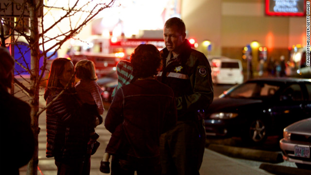 A law enforcement officer talks to people waiting outside the mall.